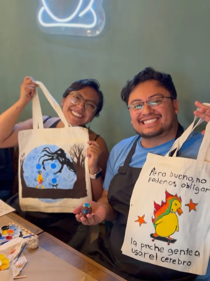 Dos asistentes muestran sus bolsas de tela pintadas en un taller de Cafairy